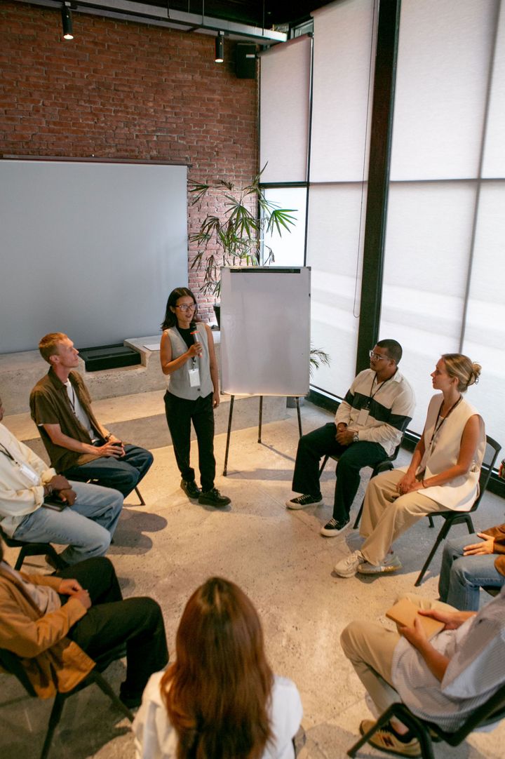 A facilitator speaks to a group of participants seated in a circle during a workshop session.